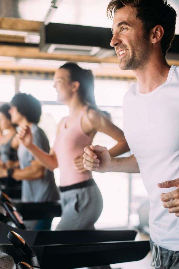People jogging on treadmills in a bright gym, smiling and enjoying their workout.